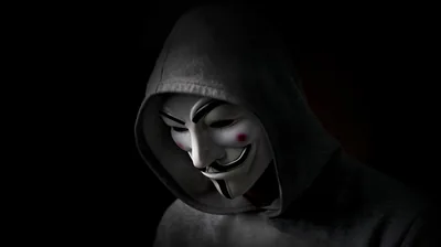 A hooded figure stands three-quarters on wearing a pale smiling mask, the shoulders lost in shadow.