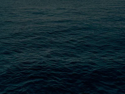 An expanse of sea at last light in a green-black teal, ripples fading with distance; dark enough overall that white widgets read anywhere.