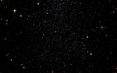 A wide field of stars with warm reds and cool blues mixed among the white, brightest along the upper edge and thinning downward.