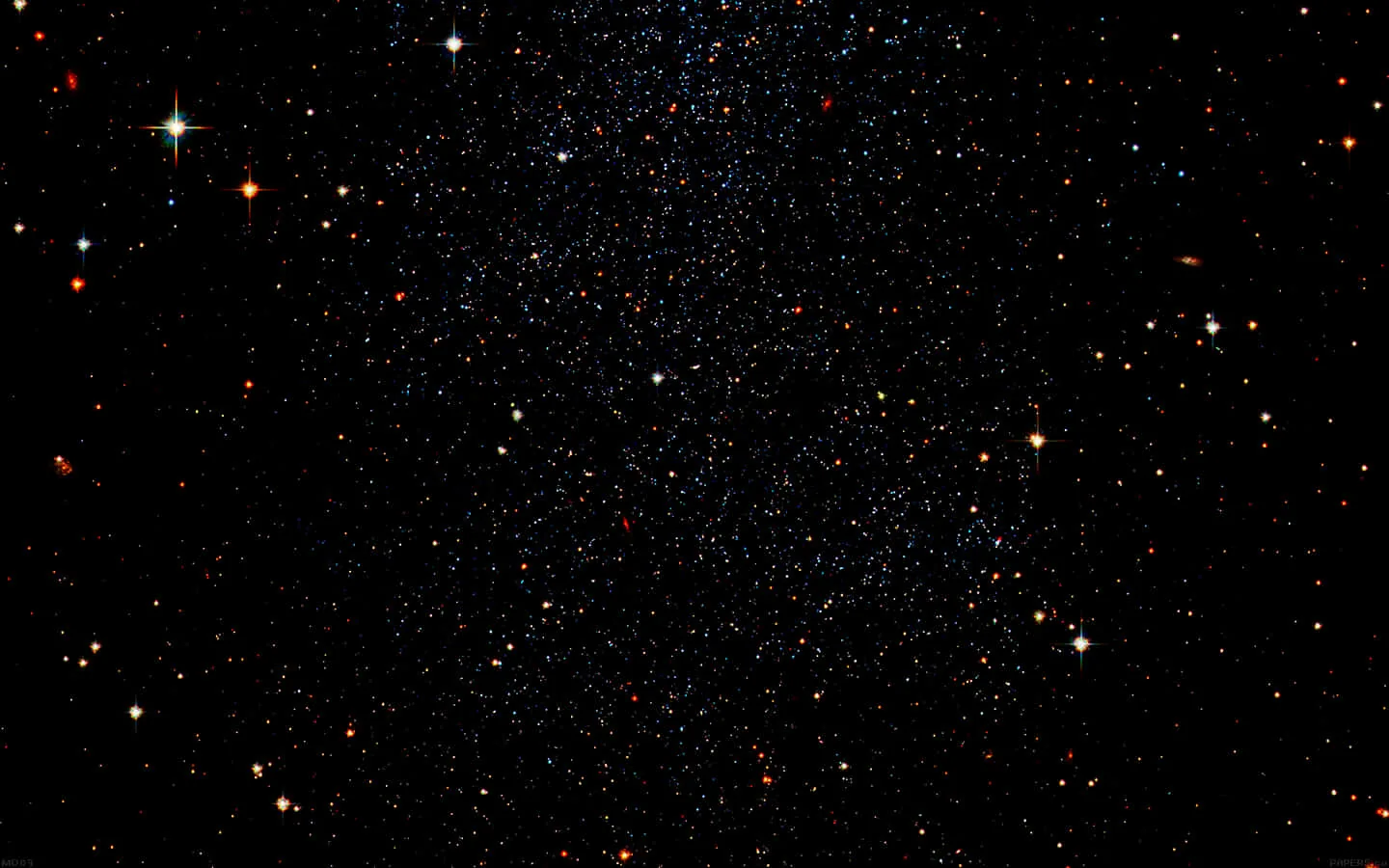 A wide field of stars with warm reds and cool blues mixed among the white, brightest along the upper edge and thinning downward.