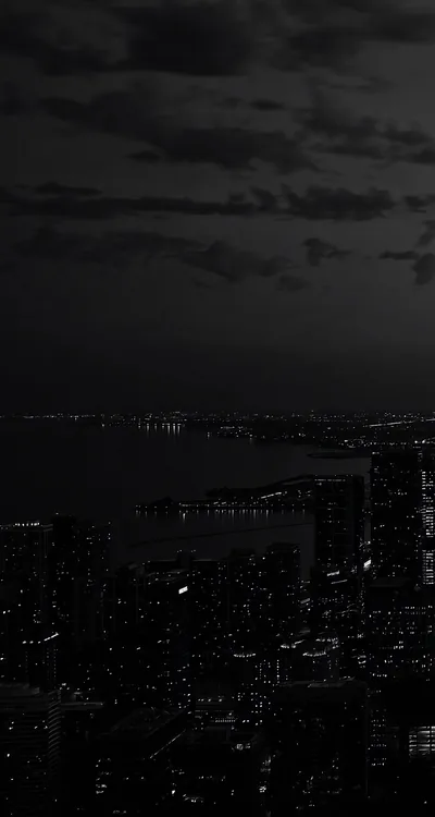 Scattered window lights trace a night skyline along a harbor, with the cloudy sky above left dark enough for the clock to sit clearly.