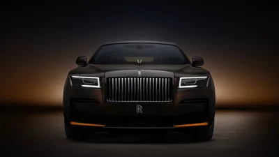 The blacked-out grille and split headlamps face the camera dead centre, an amber halo glowing behind the car and fading to black at the corners.