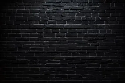 Wide courses of black brick with light spilling down from overhead, the mortar lines still readable through the middle before the corners go dark.
