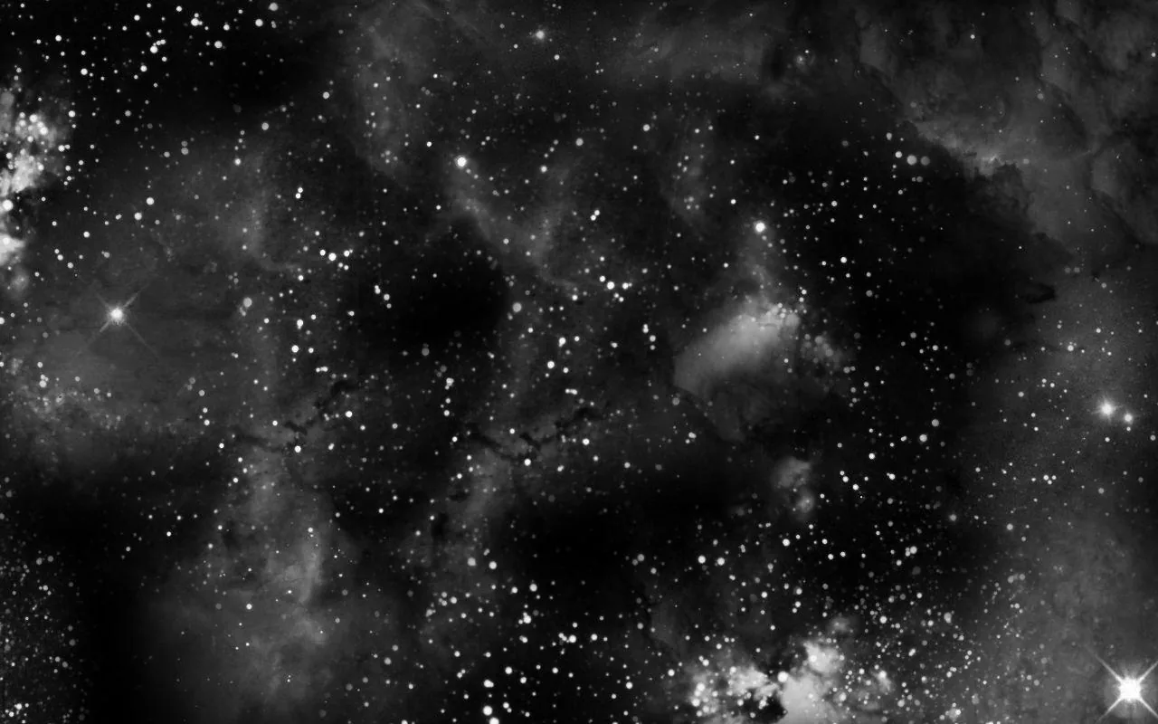 Grainy grey cloud fills the frame behind a thick spread of white stars, the darkest patches gathering along the top edge.