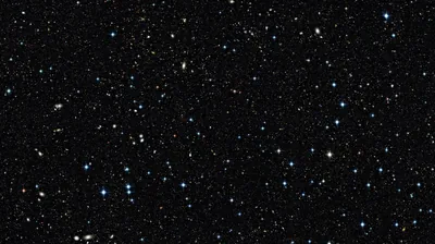 Hundreds of faint stars and fuzzy galaxies speckle a pure black field, the tiny blue and amber points spread so evenly that icons stay readable anywhere.