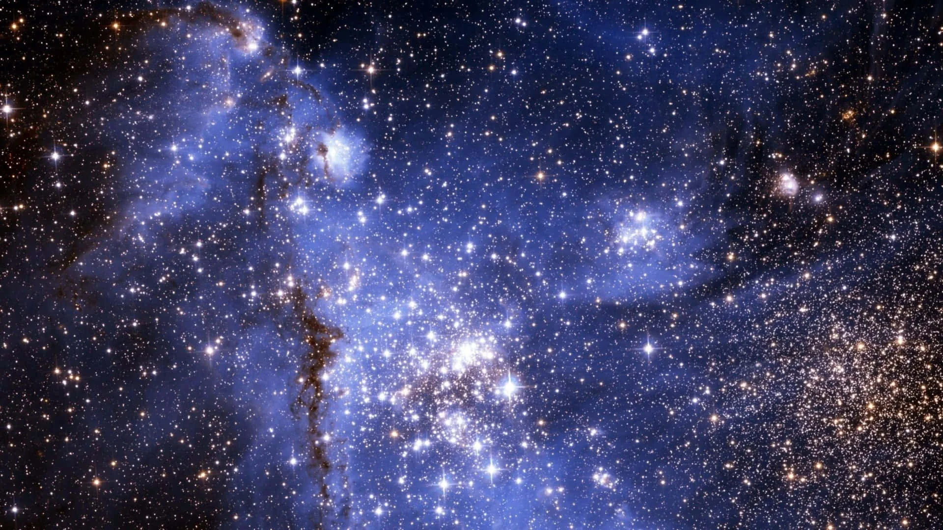 A tight cluster of young blue stars sits at the heart of glowing nebula gas, with a dark dust lane curling down the left side.
