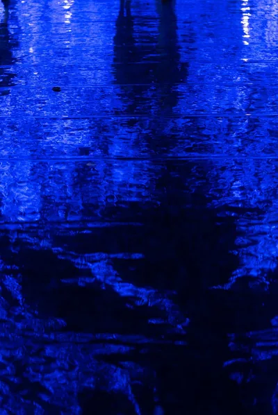 Wet ripples catch deep indigo light with tall dark shapes reflected from above, the lower half murky enough that white icons stay easy to read.
