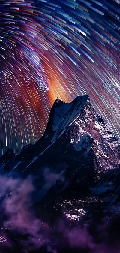 Long circular star trails sweep over a jagged dark peak, an orange glow breaking through the streaks just above the summit.