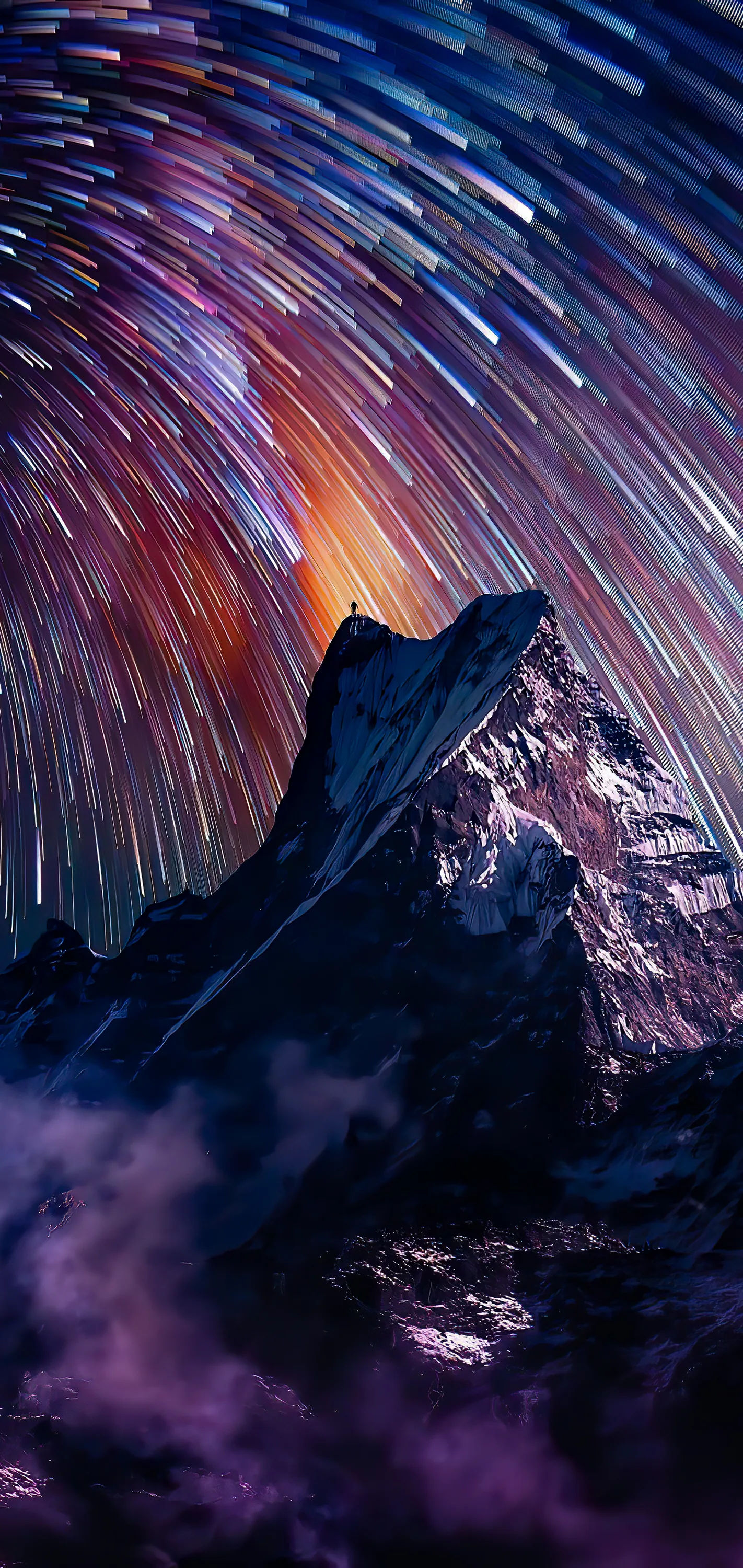 Long circular star trails sweep over a jagged dark peak, an orange glow breaking through the streaks just above the summit.