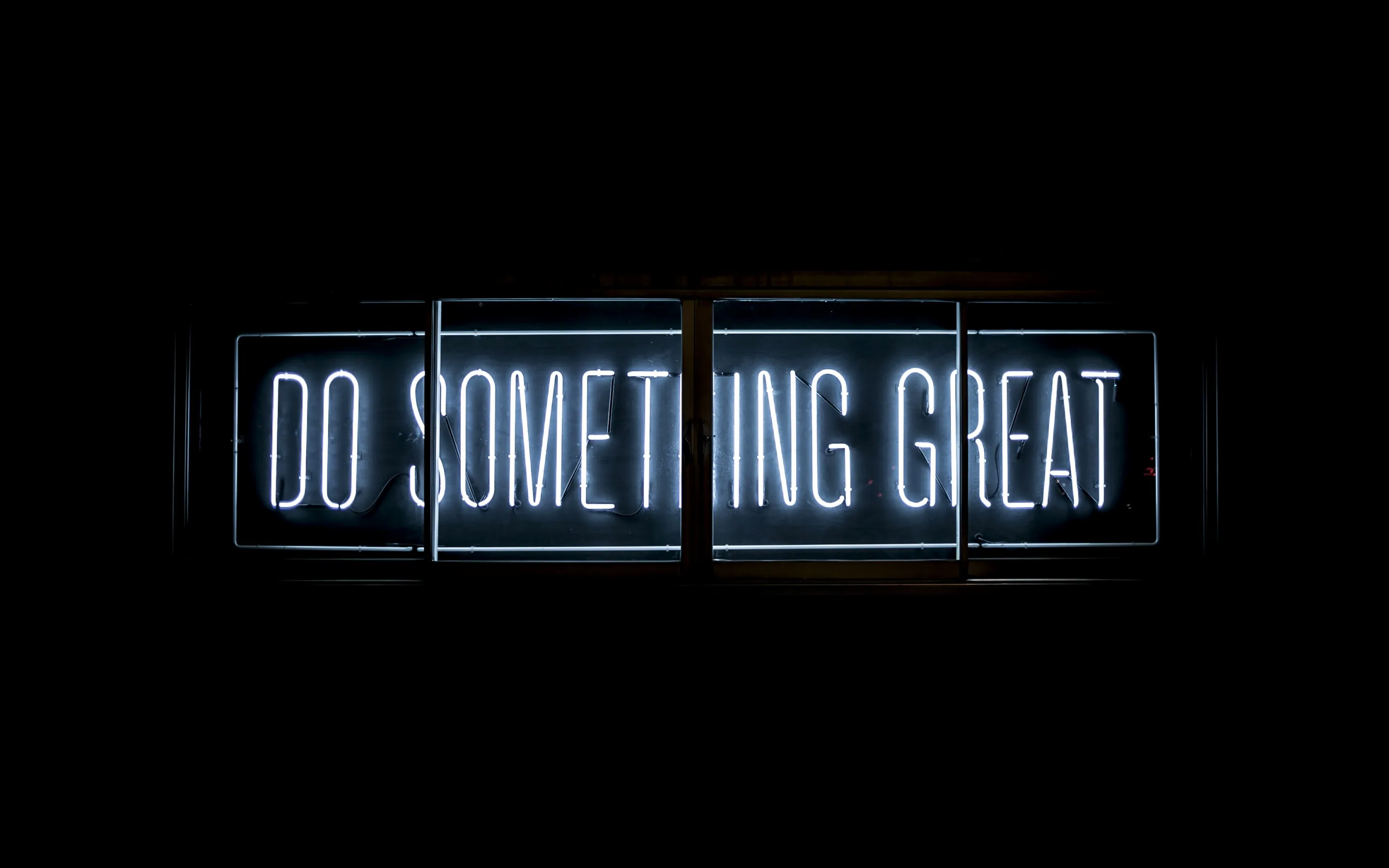 Three lit panels spell out a short phrase in cool white neon, the surrounding wall dropping straight to black.