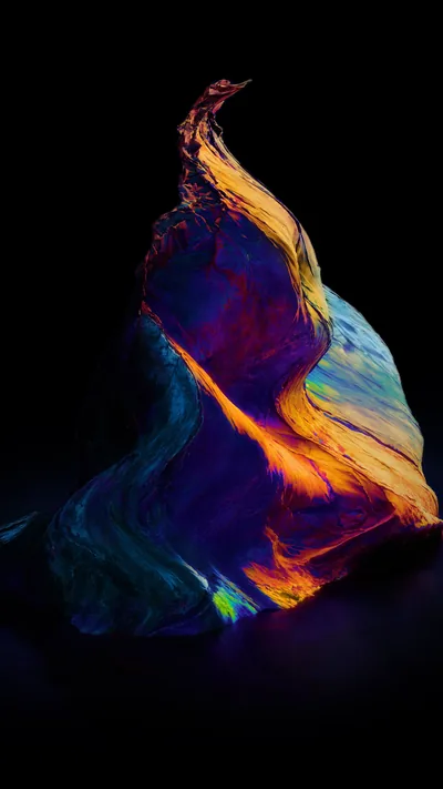 A twisted sheet of cloth catches orange, blue and green light as it rises through a tall black frame, its tip curling over to the left.