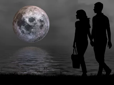 Two silhouettes hold hands at the water's edge while a large moon lays a broken silver reflection across the sea.