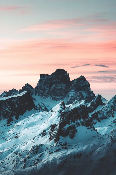 Dark rock towers streaked with snow stand under a pastel pink sky, the calm upper third keeping a phone clock easy to read.