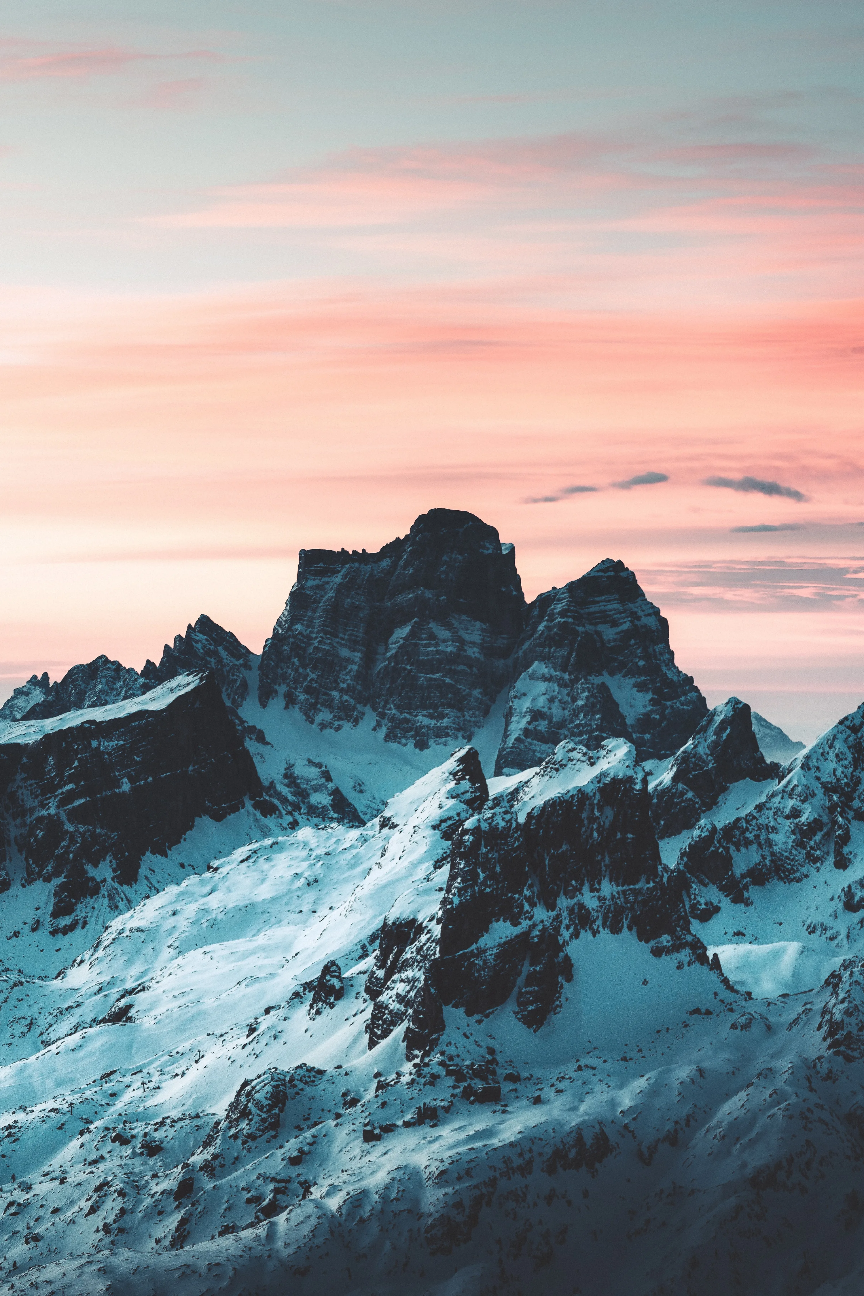 Dark rock towers streaked with snow stand under a pastel pink sky, the calm upper third keeping a phone clock easy to read.