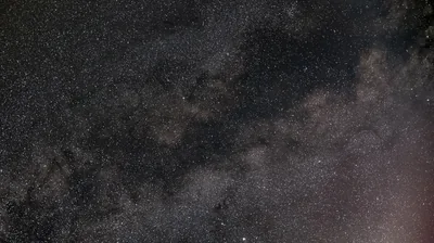 The galaxy's dark dust lane runs diagonally through a muted brown-grey sky, a faint pink glow creeping in at the lower right.