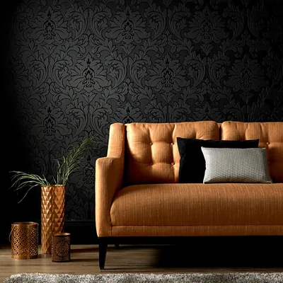 Burnt-orange tufted sofa set against a tone-on-tone black damask wall, the pattern catching light only on the right half of the frame.
