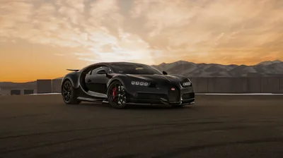 The Chiron rolls across bare tarmac as the sun drops behind a mountain ridge, orange sky filling the top half and red calipers showing through gold wheels.