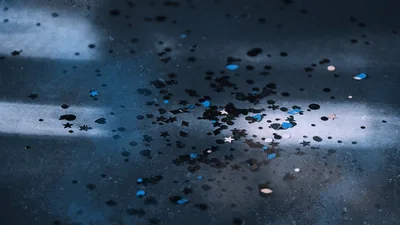Small blue and black chips scatter across a scratched grey surface, two bands of light crossing behind them.