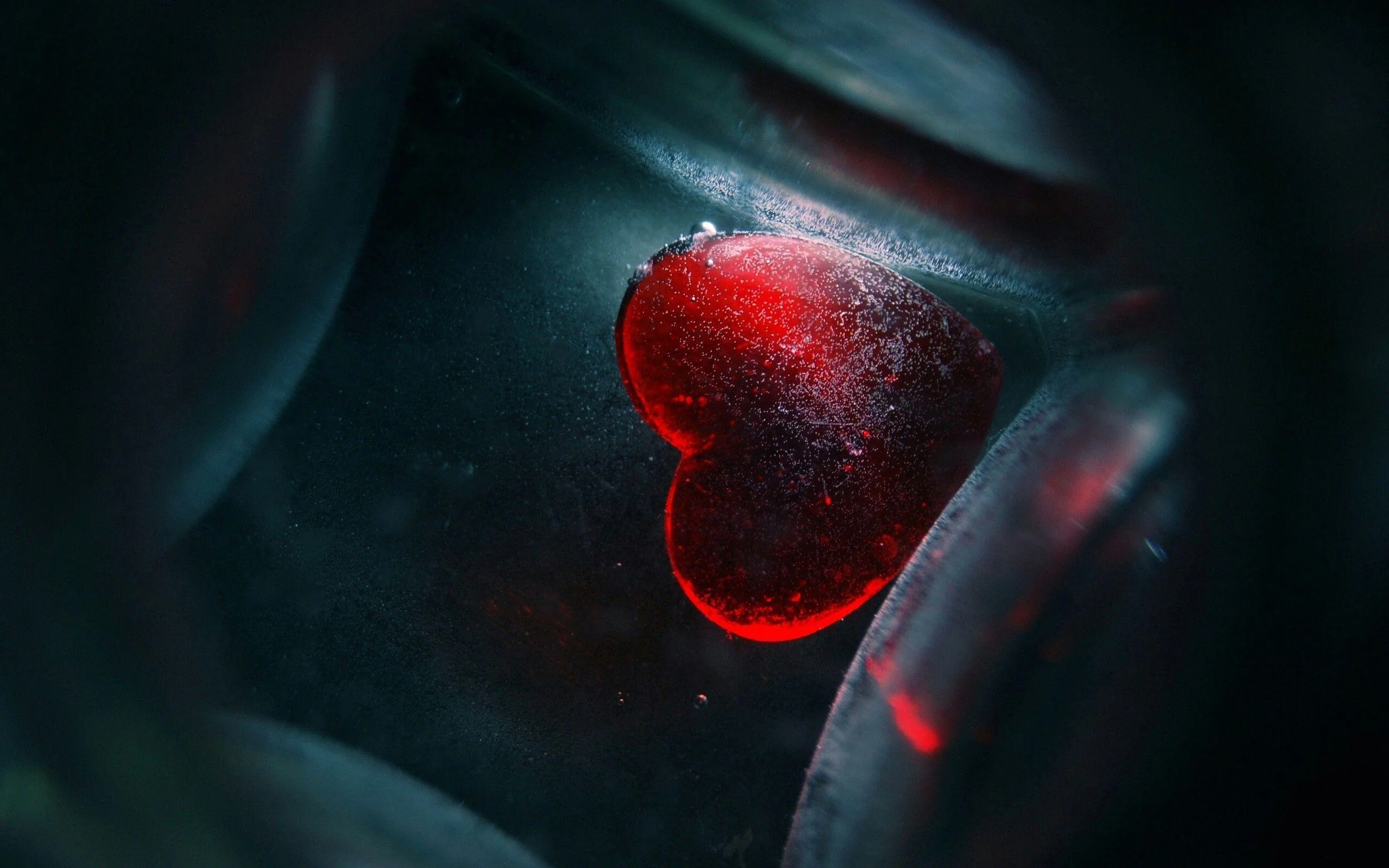 A translucent red heart glows through smoky glass, its edge fogged with condensation and the rest of the close-up dropping into shadow.