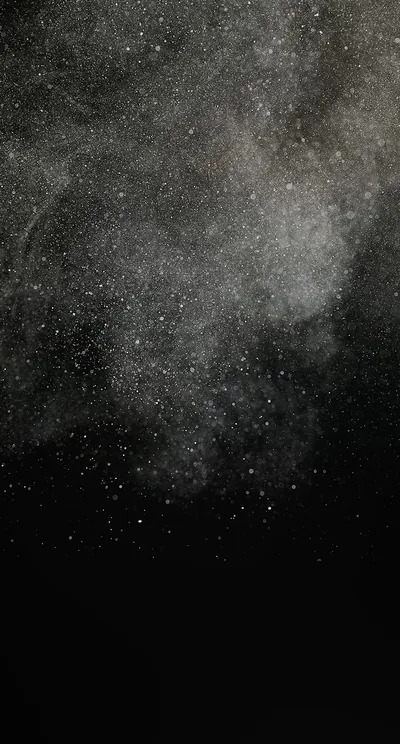 A burst of pale grey powder hangs in the upper frame, individual specks scattering out before everything drops to black.