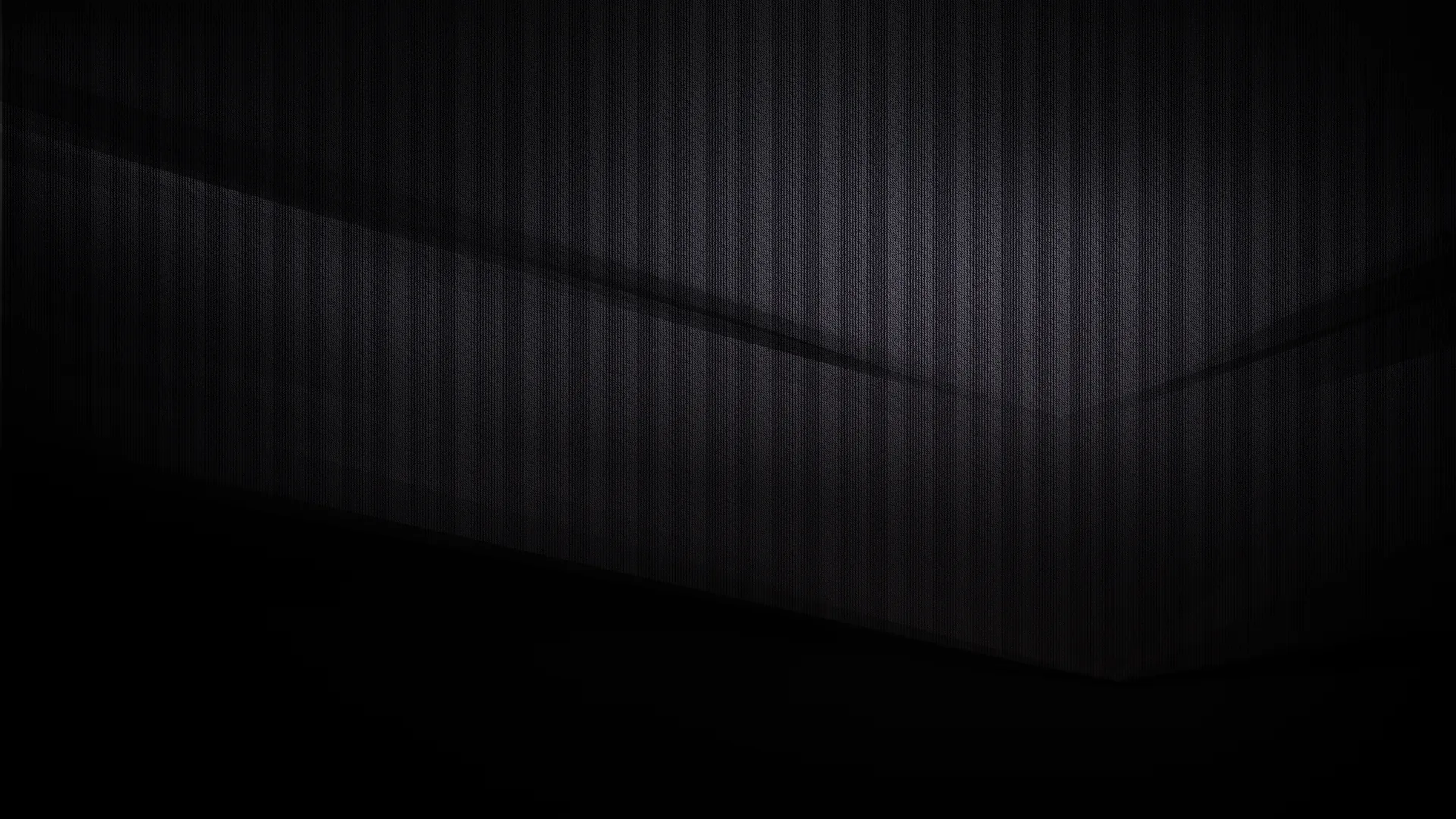 Two flat charcoal surfaces meet in a soft diagonal seam, the light just catching the fold where they join.