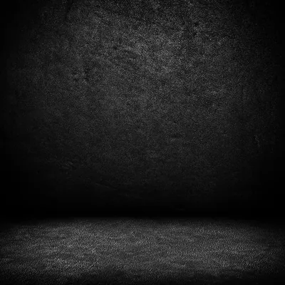 A bare studio corner where a soft overhead beam hits the back wall and spreads across the rough floor, the sides dropping to solid black.