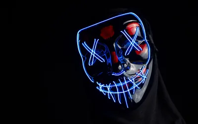 A stitched purge-style mask glows with blue electroluminescent wire under a black hood, the right side of the frame in full shadow.