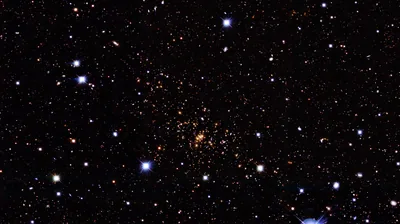 A loose cluster of amber stars sits at dead centre among white and blue pinpoints, a small blue nebula wisp entering at the bottom right corner.