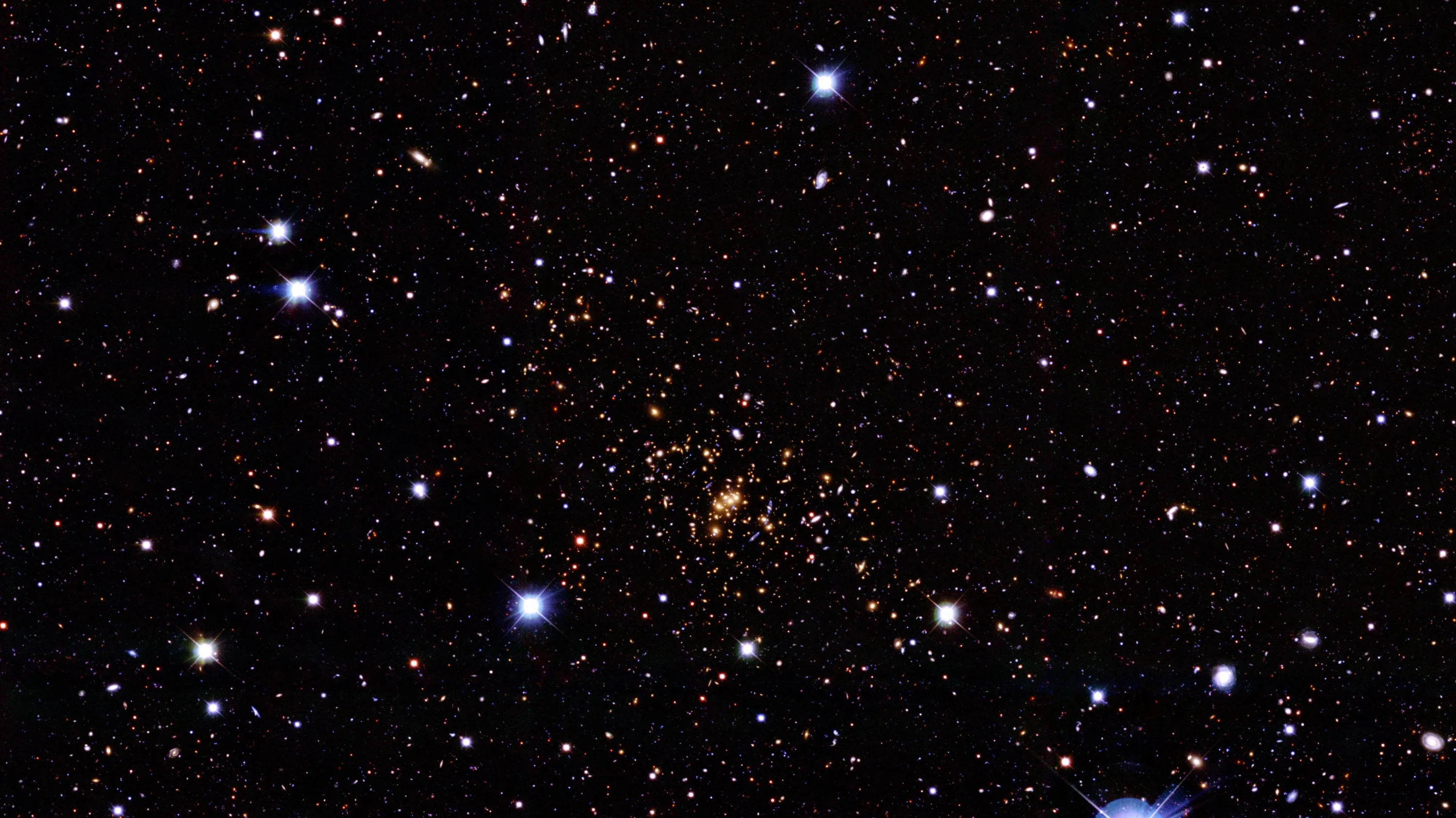 A loose cluster of amber stars sits at dead centre among white and blue pinpoints, a small blue nebula wisp entering at the bottom right corner.