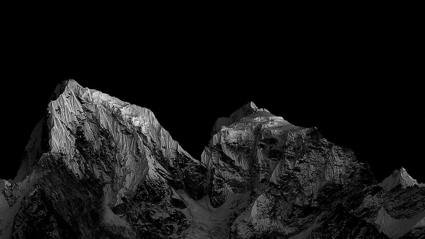 Two ridged summits catch a cold sidelight in monochrome while the sky above them drops to solid black, leaving the top half empty.