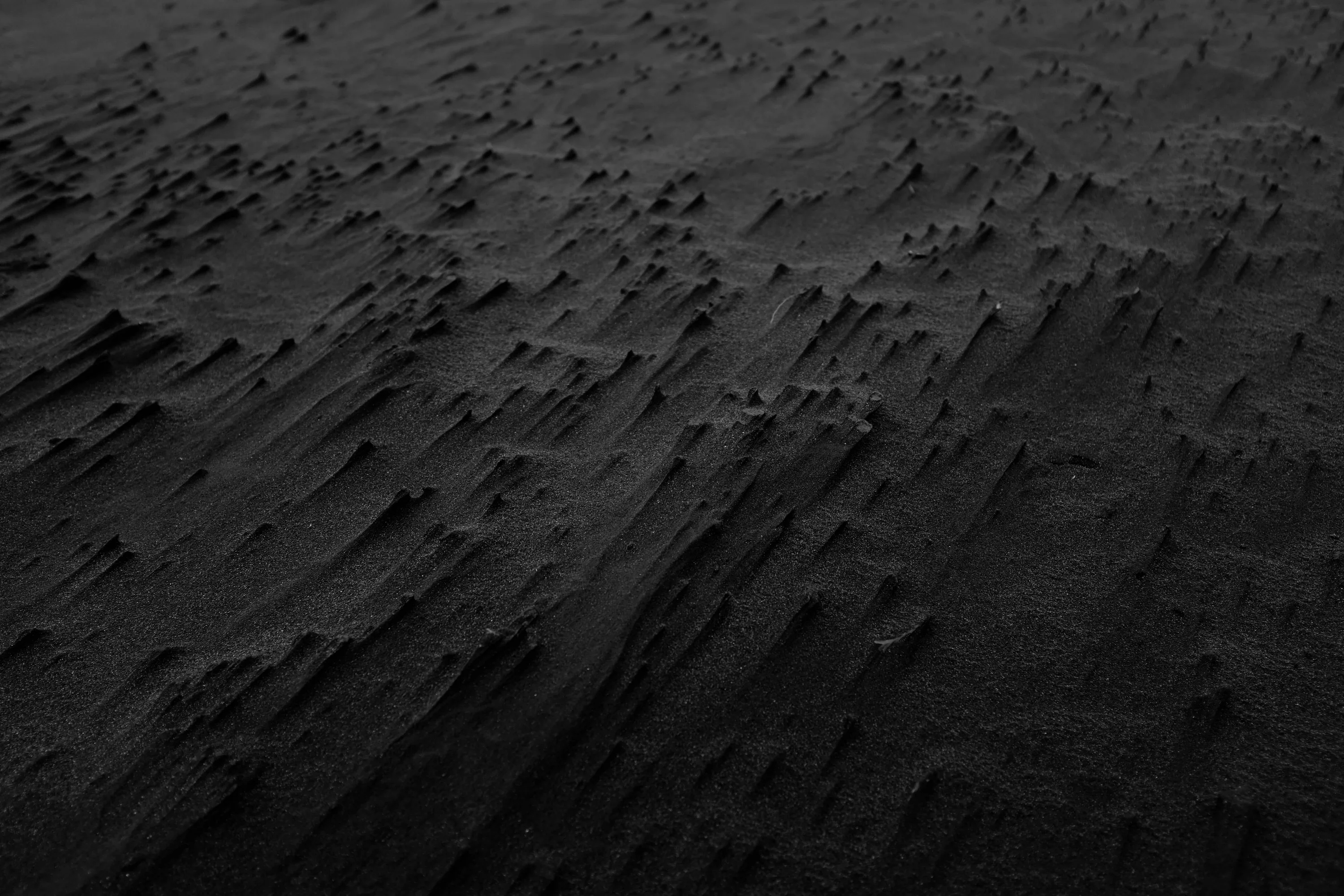 Wind-cut ridges run diagonally across dark volcanic sand, the texture sharpest in the lower half of the frame.