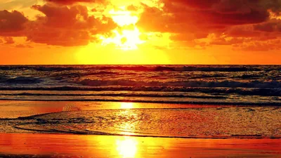 The sun burns through torn clouds and turns sea, foam and wet beach into one sheet of amber, with barely any other colour in the frame.