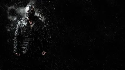 Bane stands to the left in his heavy coat and mask as rain streaks across the frame, the whole right half left dark and open.