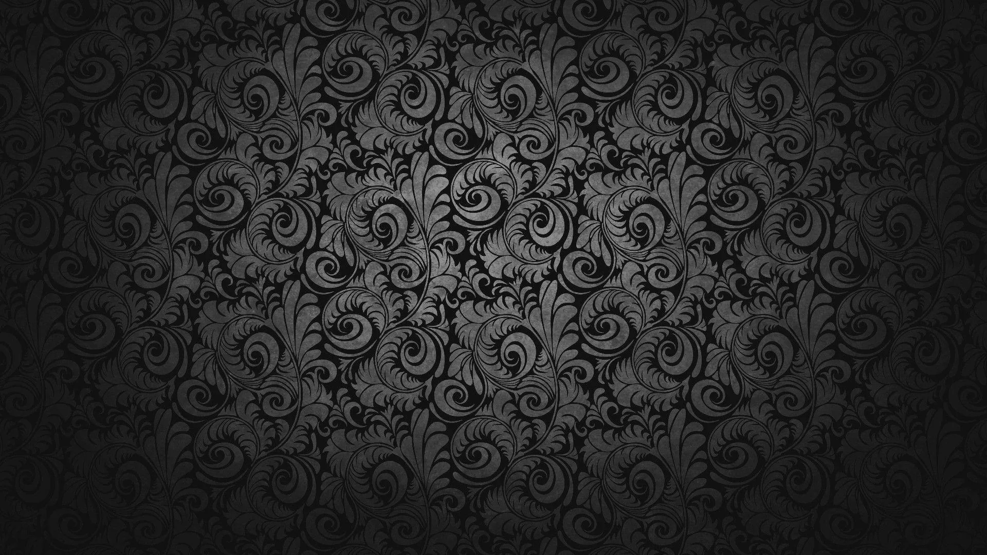 A repeating damask scroll covers a charcoal wall in low relief, lit from the centre so the pattern sinks into black around all four edges.