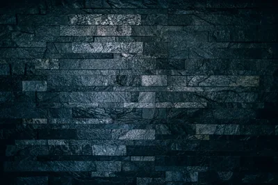Thin slate bricks stack in uneven courses, cool blue light washing the upper middle while the edges stay in deep shadow.