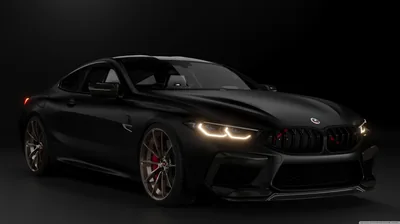 Front three-quarter of a widebody M8 under low studio light, its laser headlights lit and bronze forged rims the only break from the black paint.