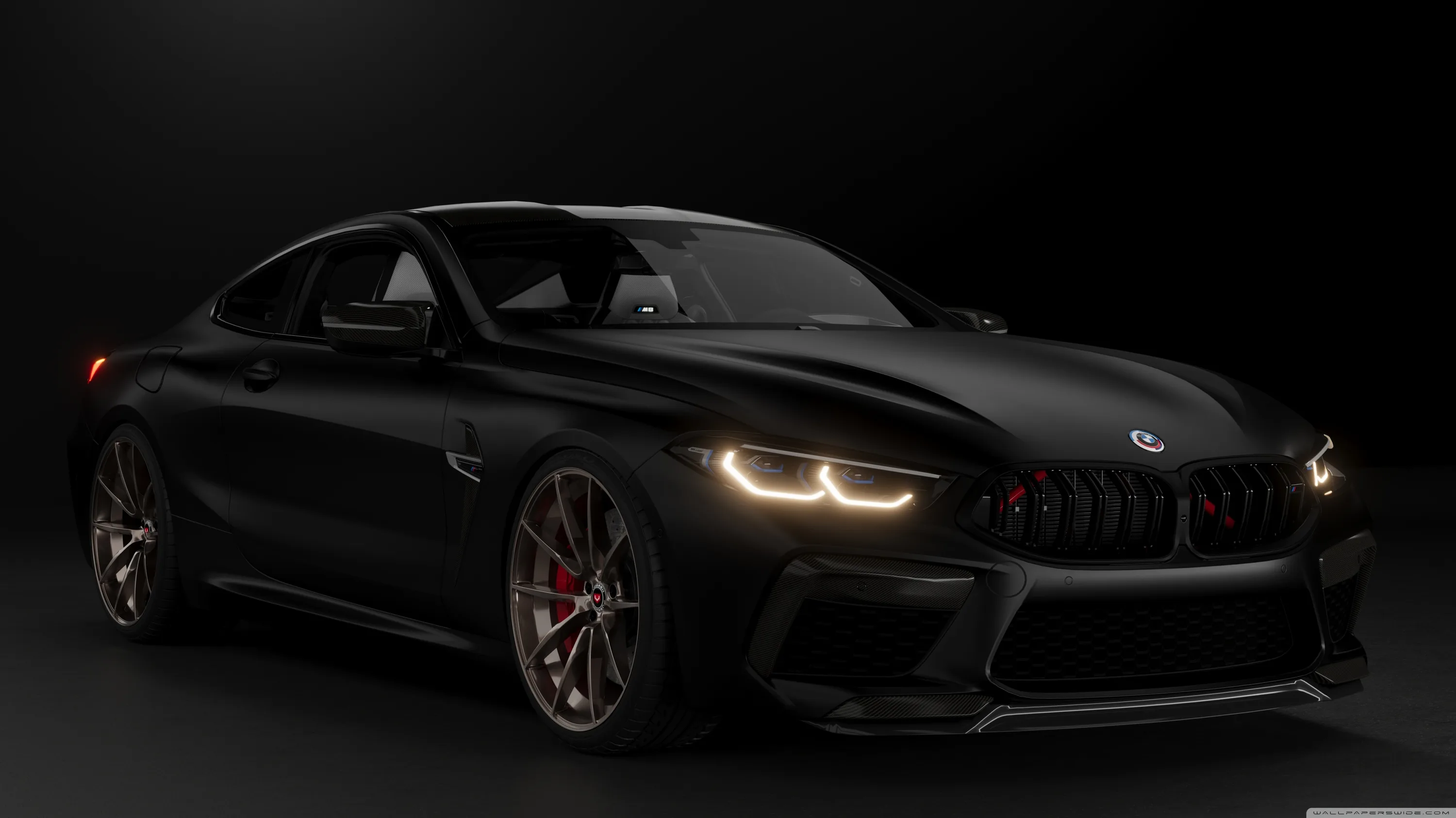 Front three-quarter of a widebody M8 under low studio light, its laser headlights lit and bronze forged rims the only break from the black paint.