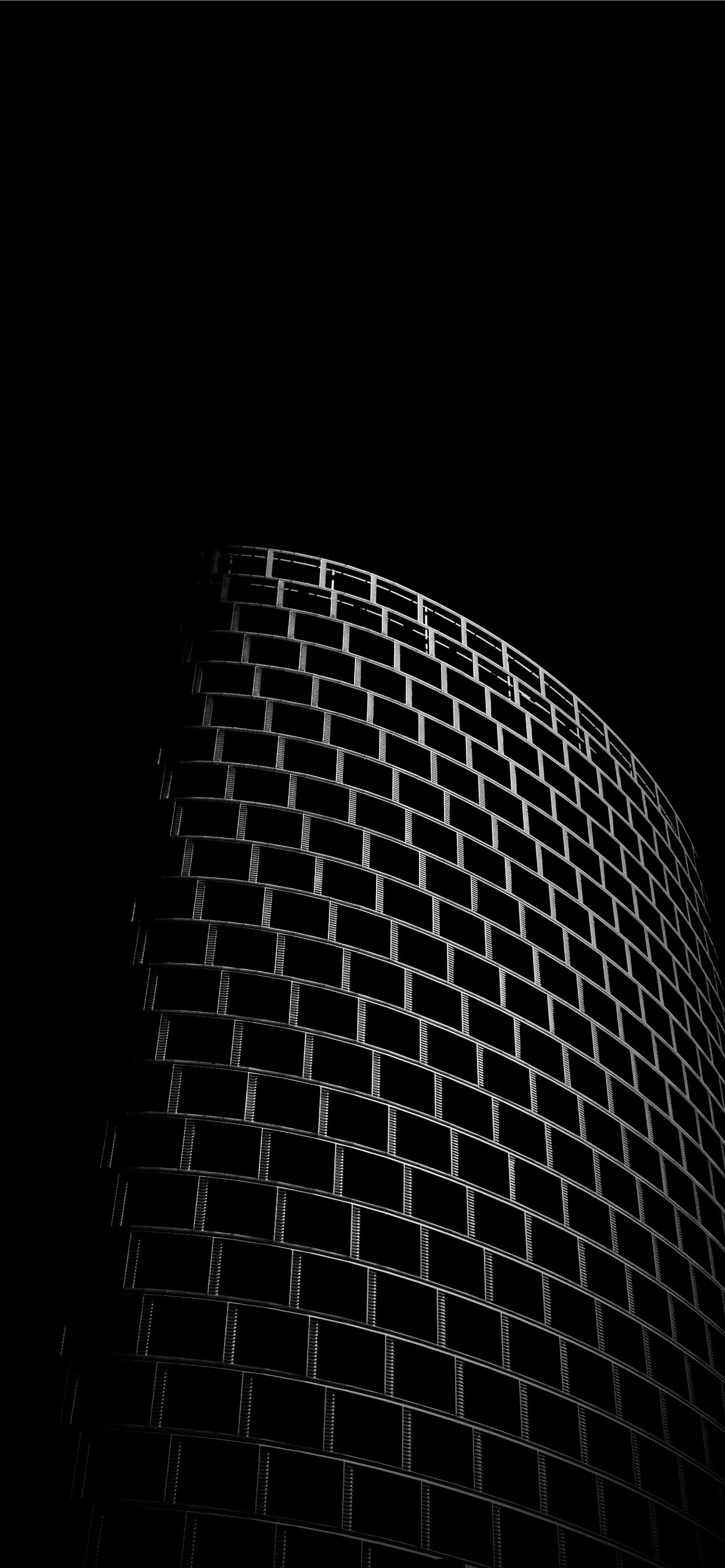 A tower's curved brick face catches a narrow band of light down one side, the sky and the rest of the wall left in full black.