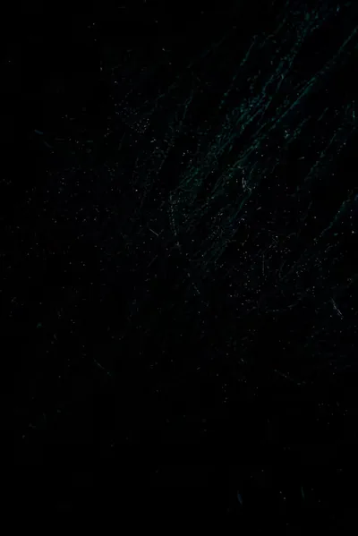 Dark stone fills a tall frame with faint green-blue veins and speckles through the upper half, the base left almost entirely black.
