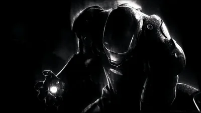An armoured suit emerges from near-total darkness, the only light coming from the glowing repulsor in its raised hand.