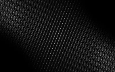 A rubber or leather surface stamped with a diamond weave curves through the frame, the light raking in from the right and the left corner in full shadow.