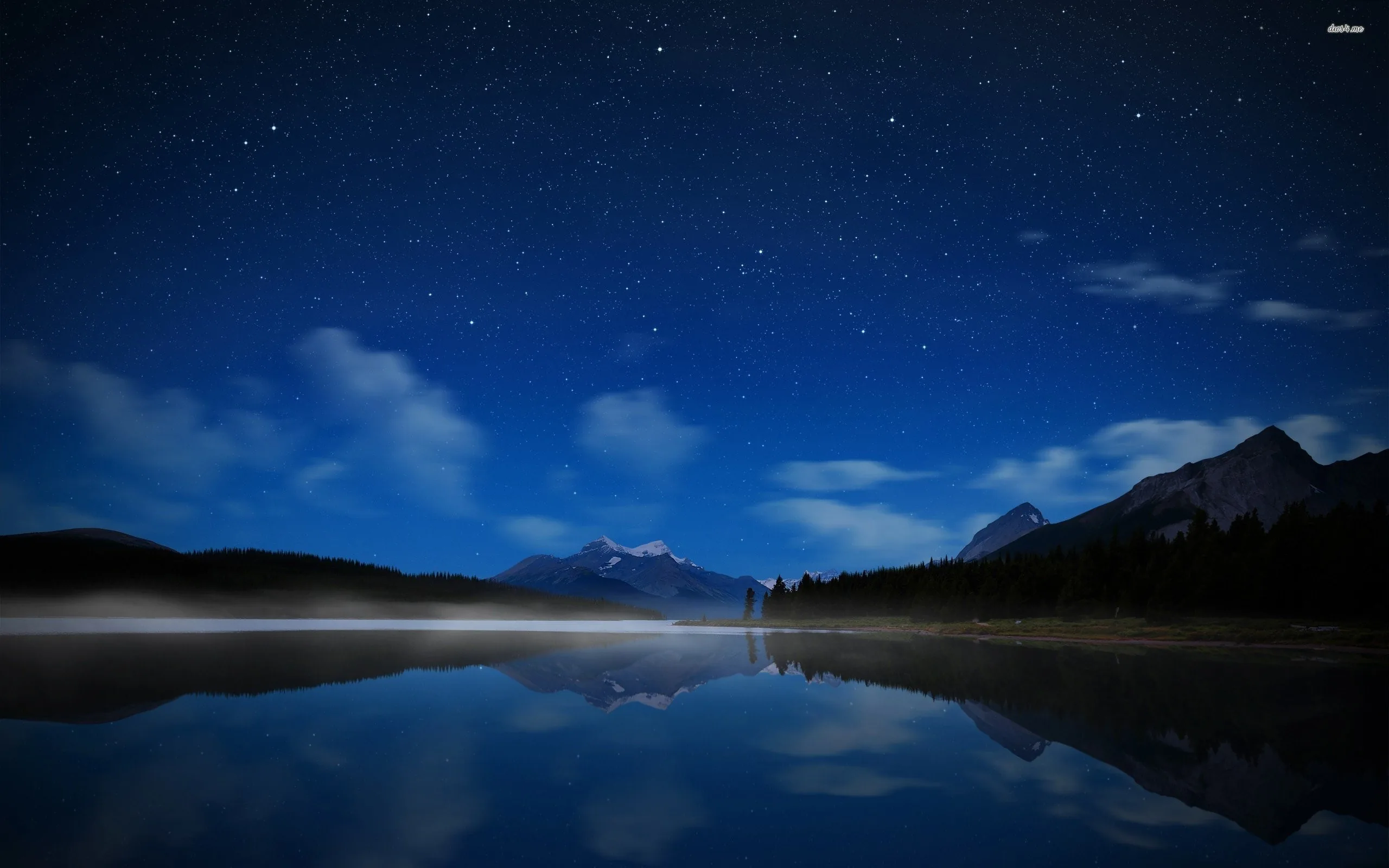Thin mist slides across a mountain lake beneath scattered stars, the far peaks and their reflection meeting along the centre line.