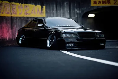 A VIP-style saloon sits on the deck with Japanese height-limit signage painted overhead, tunnel light falling on the bumper and chrome lip wheels.