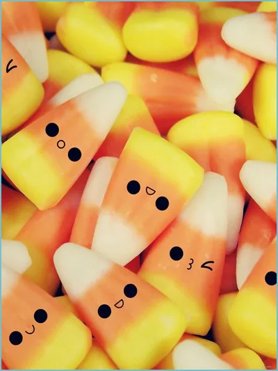 Real candy corn pieces photographed close up, each drawn over with a tiny inked face; the sharpest sweets sit centre left while the edges blur away.