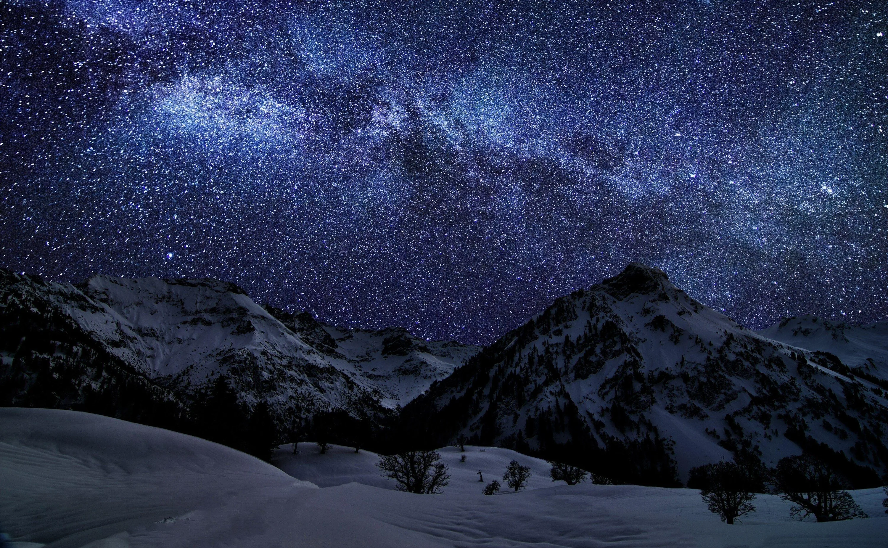 A dense white starfield with a faint Milky Way band fills the sky above a black pyramid peak, untouched snowfields catching starlight below.
