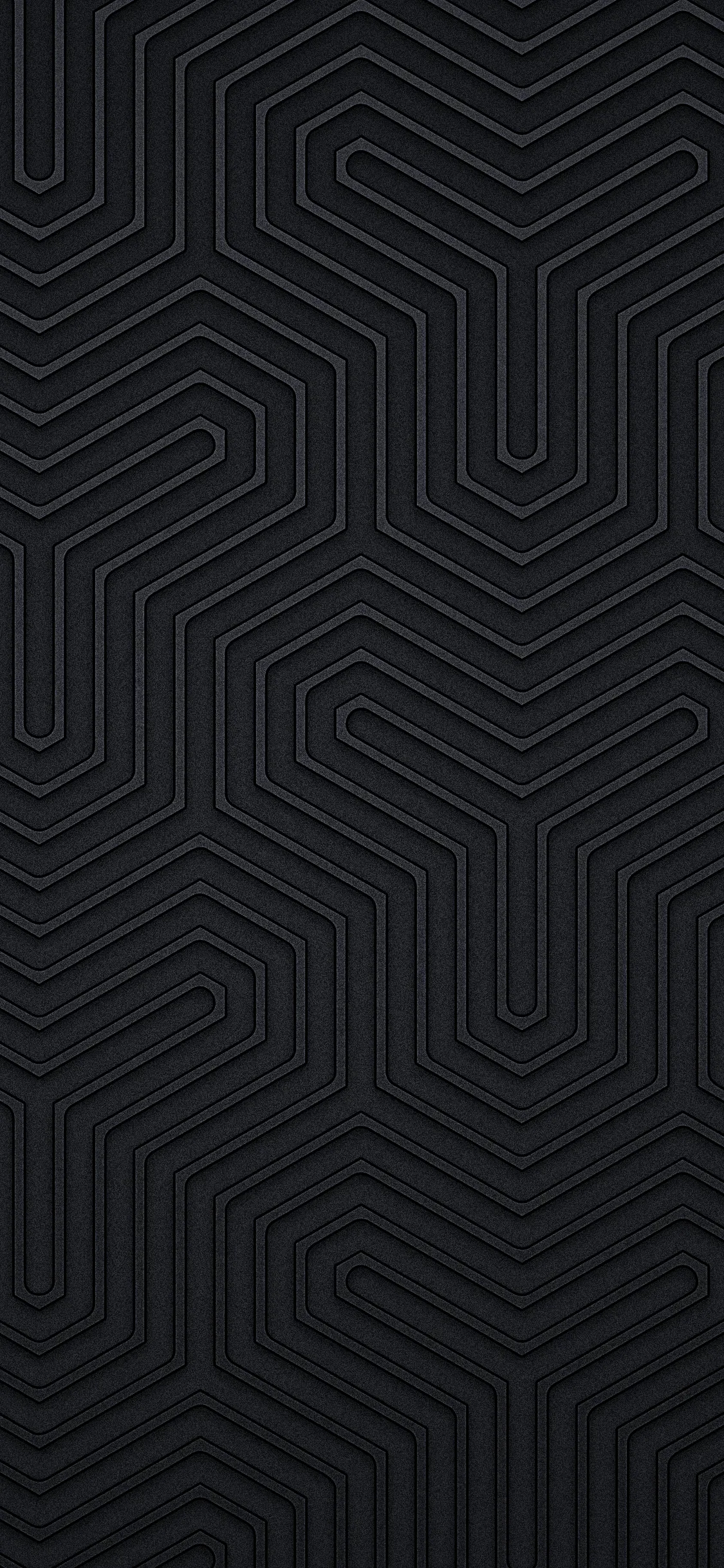 Concentric hexagonal grooves interlock like a labyrinth down the tall frame, each ridge picking up a thin highlight against matte charcoal.