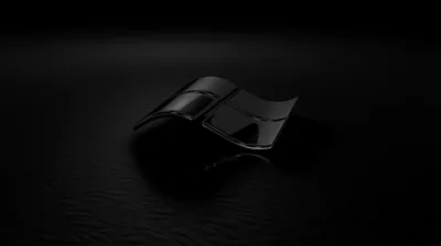 The four-pane Windows flag sits in dark glass on a matte floor, one weak spotlight from above catching its top edge and nothing else.