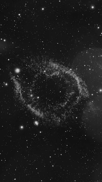 A faint circular shell of gas sits slightly left of centre, ringed by bright foreground stars in a grainy greyscale exposure.