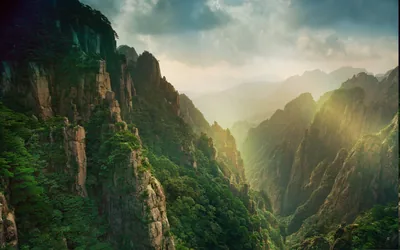 Rays fan through haze between forested stone pinnacles in a Chinese canyon, the bright break in the clouds drawing the eye to the centre of the frame.