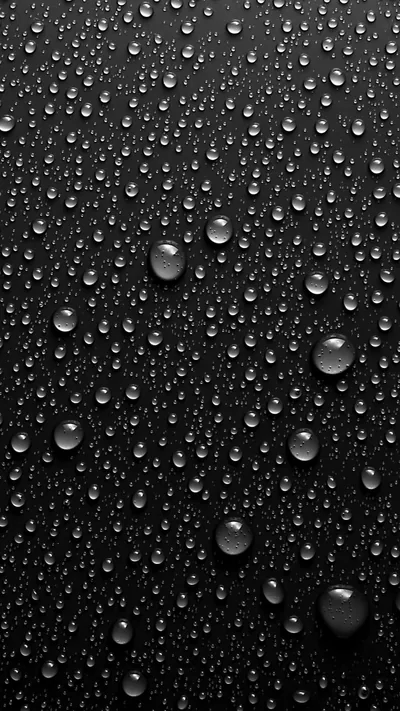Condensation beads across a black glass surface, a few larger drops in the lower half sliding down and leaving faint trails.